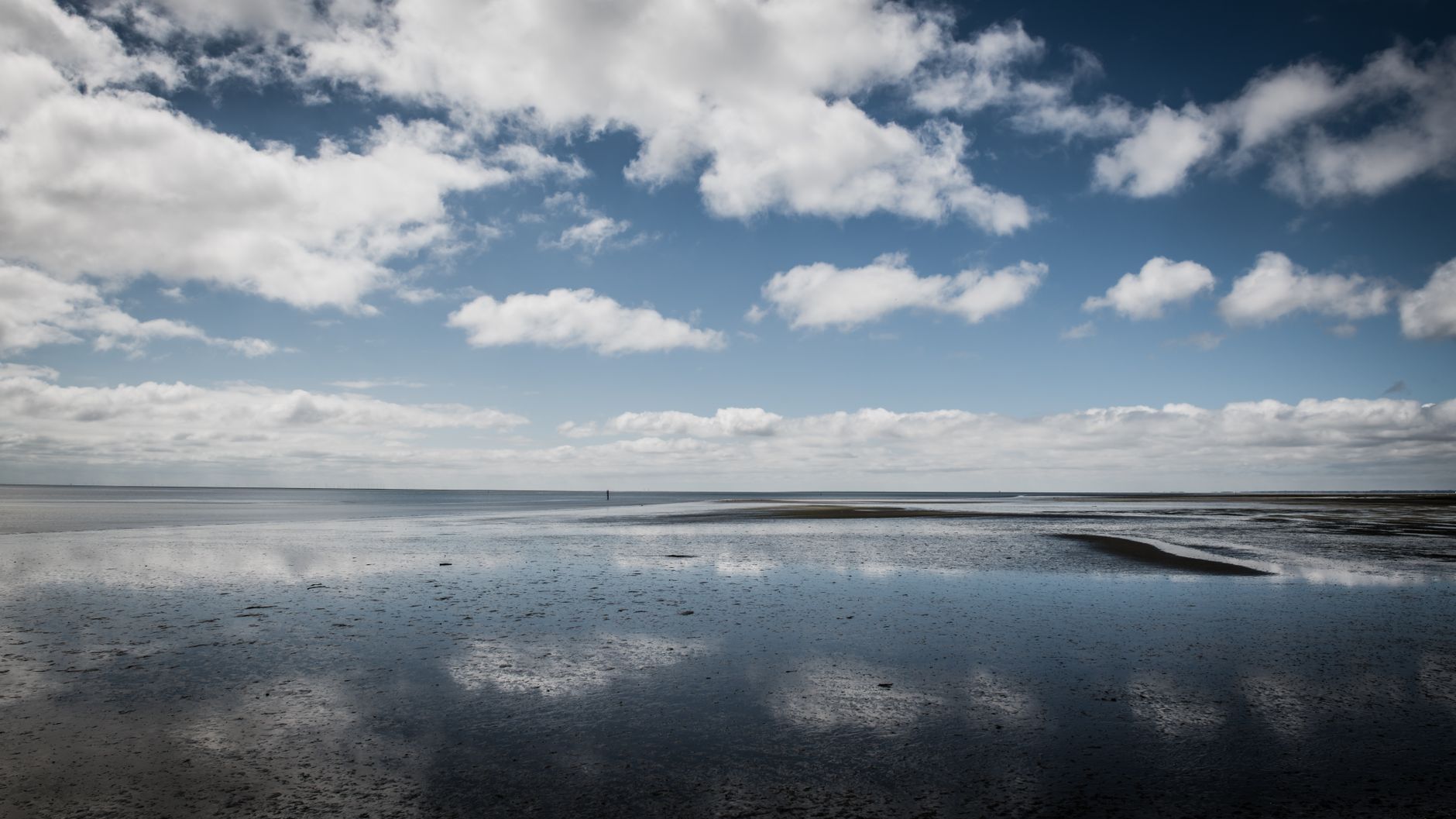Peaceful beach with clouds reflecting on calm waters at Rømø, Denmark.