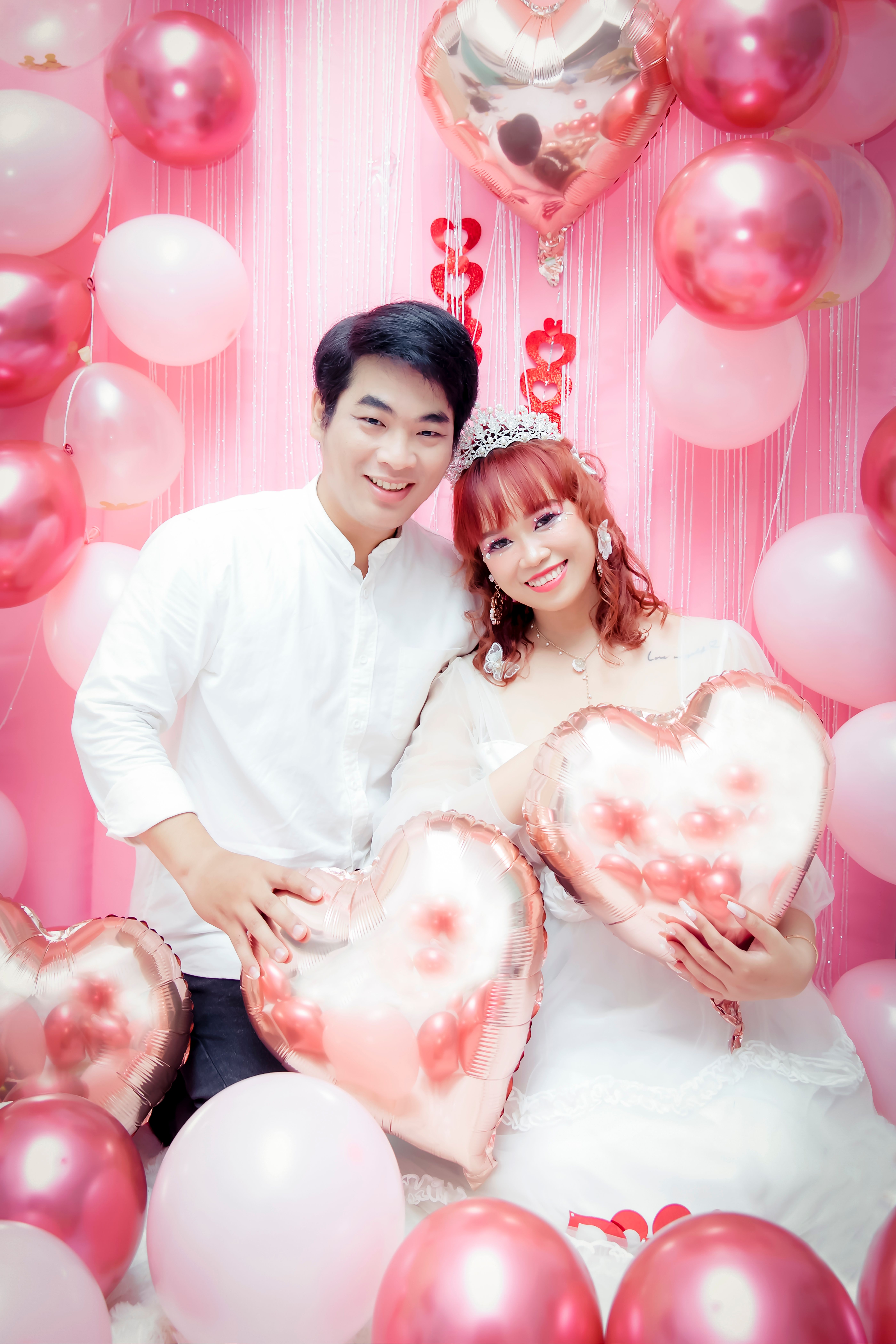 A happy bride and groom surrounded by pink balloons, capturing joyful wedding moments in a studio setting.