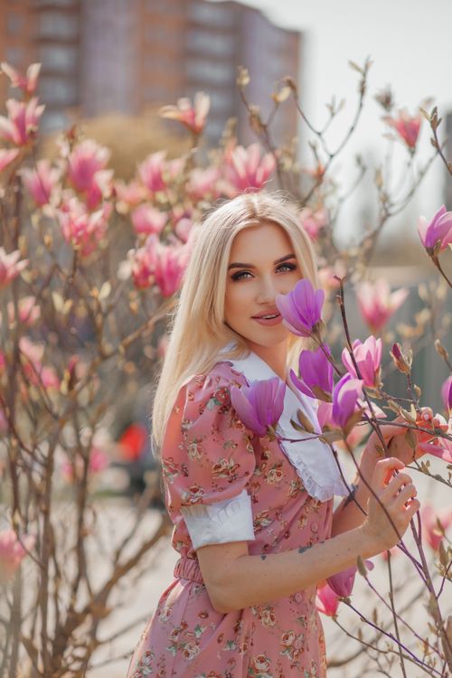 Free A young woman in a floral dress smiles among blooming magnolia trees in the spring sunlight. Stock Photo