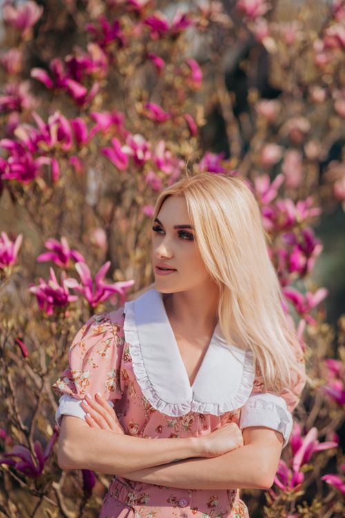 Free A beautiful blonde woman in a floral dress posing among vibrant pink flowers in a natural setting. Stock Photo