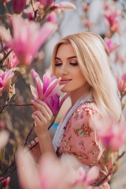 Free Beautiful blonde woman enjoying pink magnolias in full bloom during summer. Stock Photo