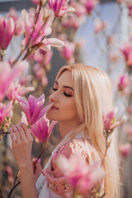 Free A serene moment of a blonde woman amongst vibrant pink magnolia flowers in spring. Stock Photo