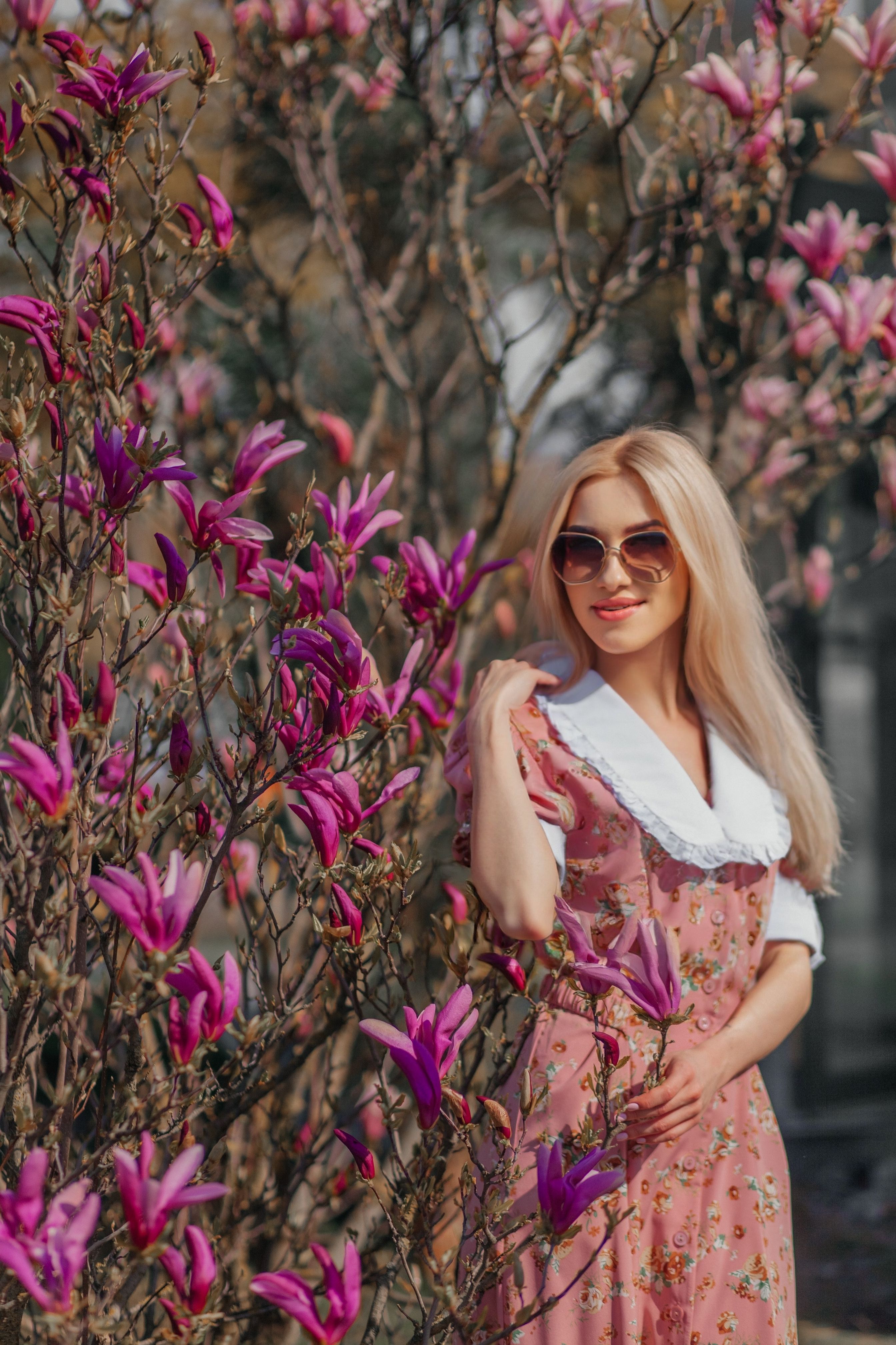 Charming woman in floral dress enjoying a sunny day in a garden of blooming pink flowers.