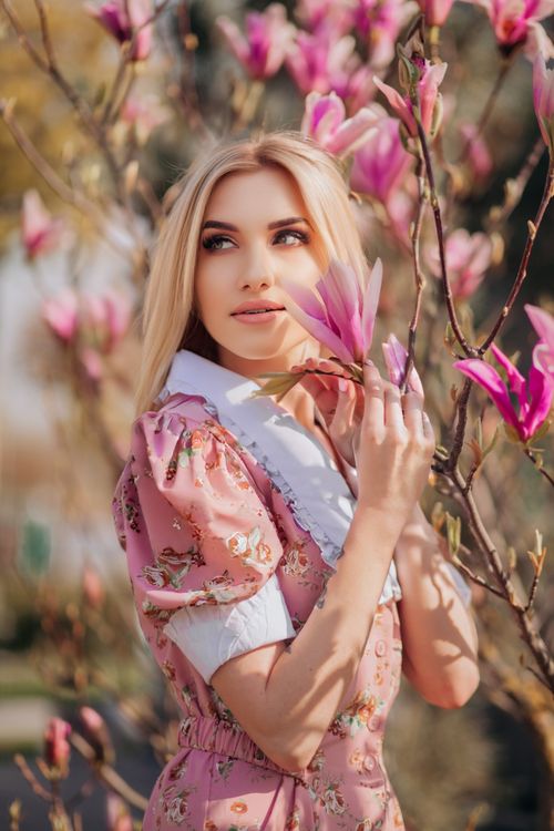 Free Elegant woman in floral dress surrounded by blooming magnolias in a sunlit park. Stock Photo