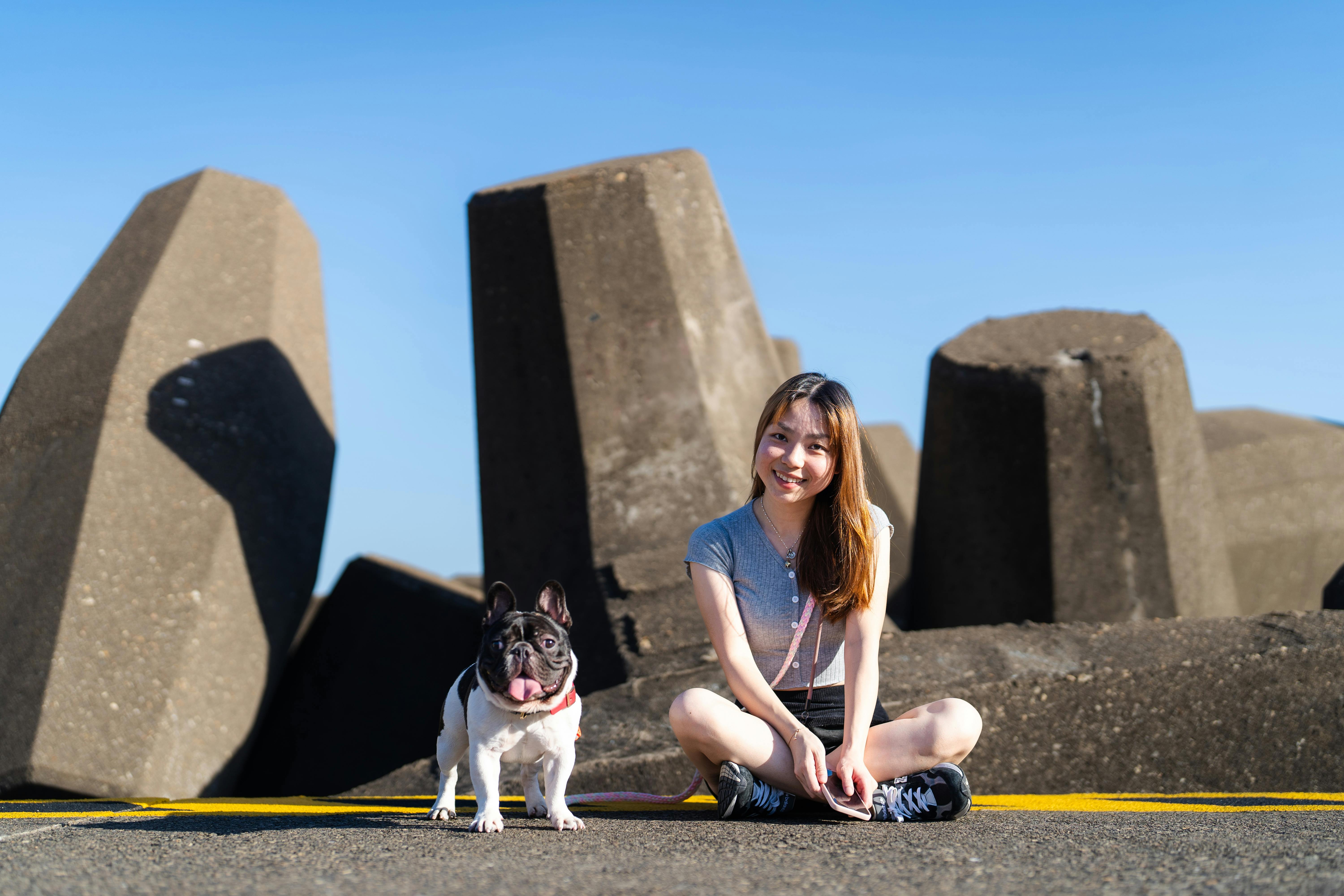 smiling teenage girl sitting with a french bulldog in front of large tetrapods