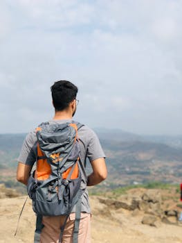 Back view of a man hiking with a backpack, enjoying the scenic view of hills in Pune, India.