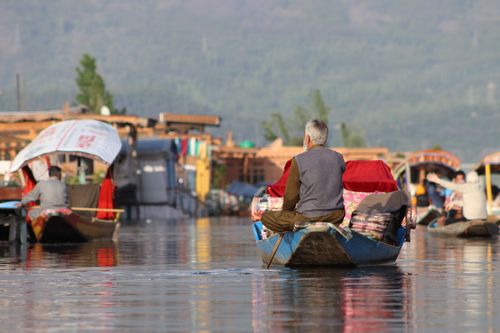 Free Elderly man sitting on a boat navigating a beautiful, calm lake, surrounded by vibrant colors. Stock Photo
