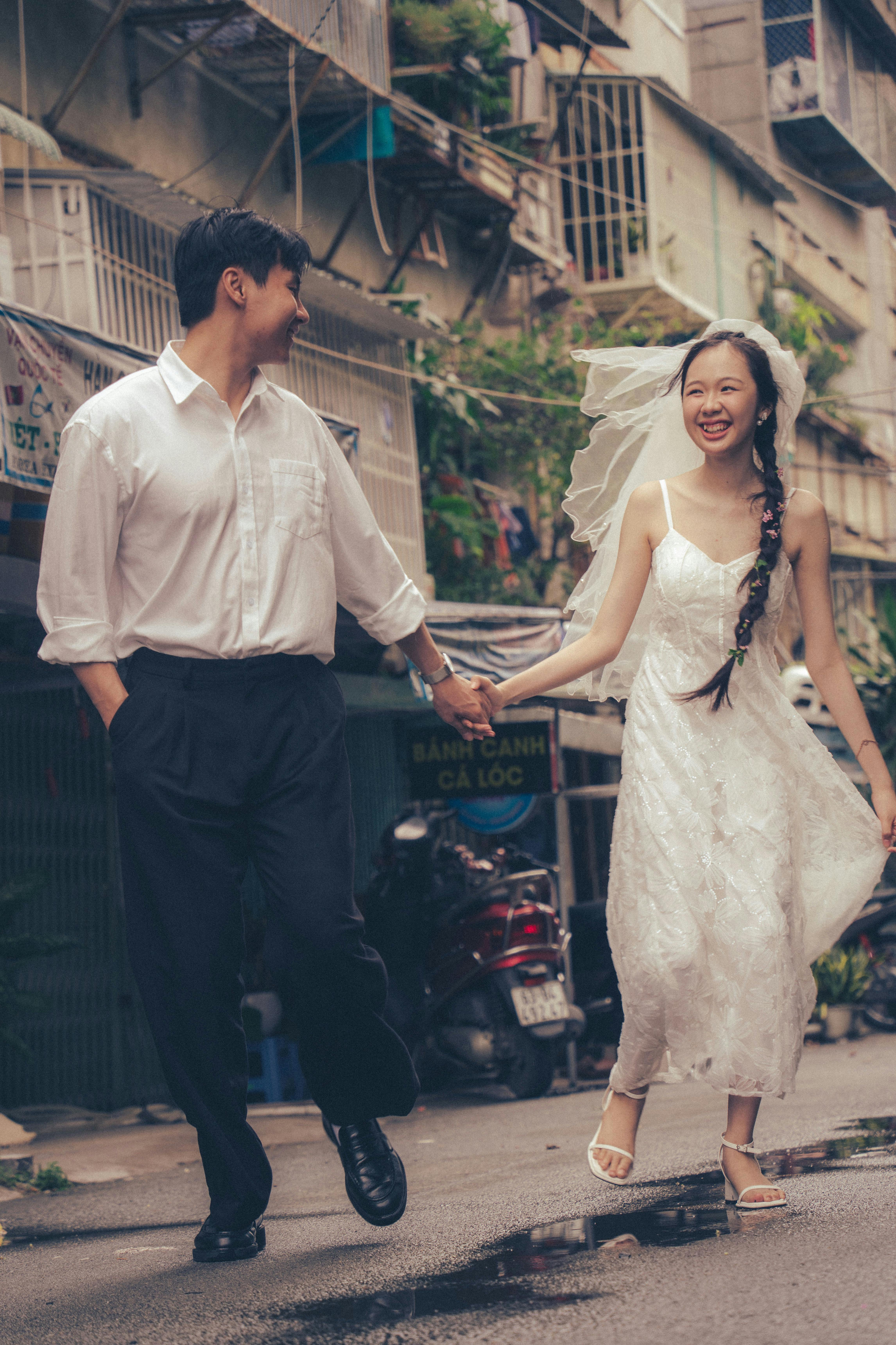 Smiling bride and groom running hand in hand on a lively city street, capturing pure joy and love.