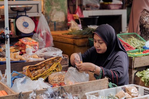 Free Indonesian market scene with a woman vendor organizing produce. Vibrant and authentic market atmosphere. Stock Photo
