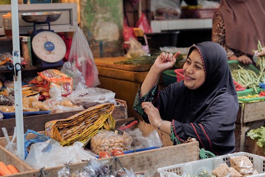 A smiling vendor in a hijab at a bustling market in Pontianak, Indonesia.