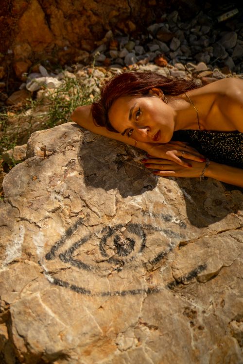 Free A serene young woman relaxes on a sunlit rock outdoors, basking in summer warmth. Stock Photo