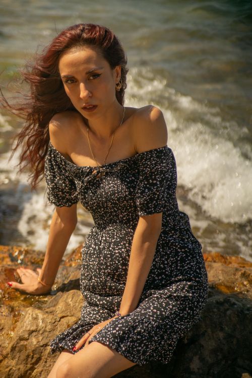 Free Young woman sitting on rocks by the sea in summer sunlight. Stock Photo
