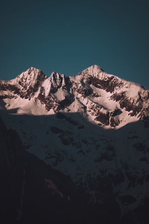 Free Dramatic shot of a snowcapped mountain peak under a blue sky during sunrise. Stock Photo