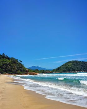 Tranquil beach with crystal blue waters and lush hills in Paraty, Brazil.