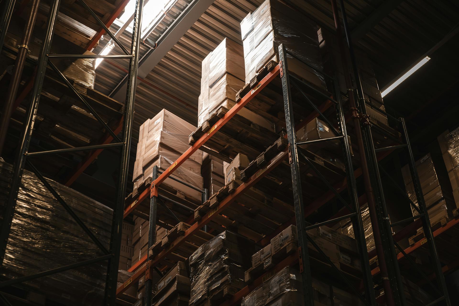 Interior view of a warehouse with stacked cardboard boxes on high shelves, showcasing storage and logistics.