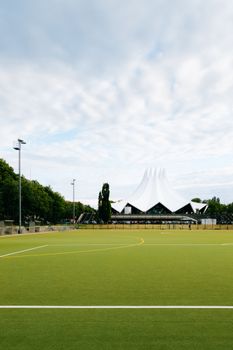 Wide view of the iconic Tempodrom in Berlin, Germany with an adjacent green sports field under a cloudy sky.