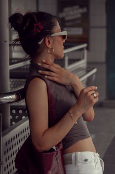 Stylish woman with hair bun and sunglasses leaning on a handrail outdoors.