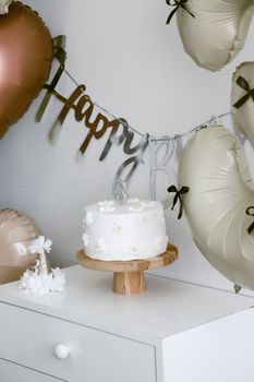A beautifully decorated birthday cake with white flowers and balloons, creating a festive atmosphere.