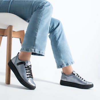 Stylish silver sneakers paired with blue jeans in a minimal indoor setting.