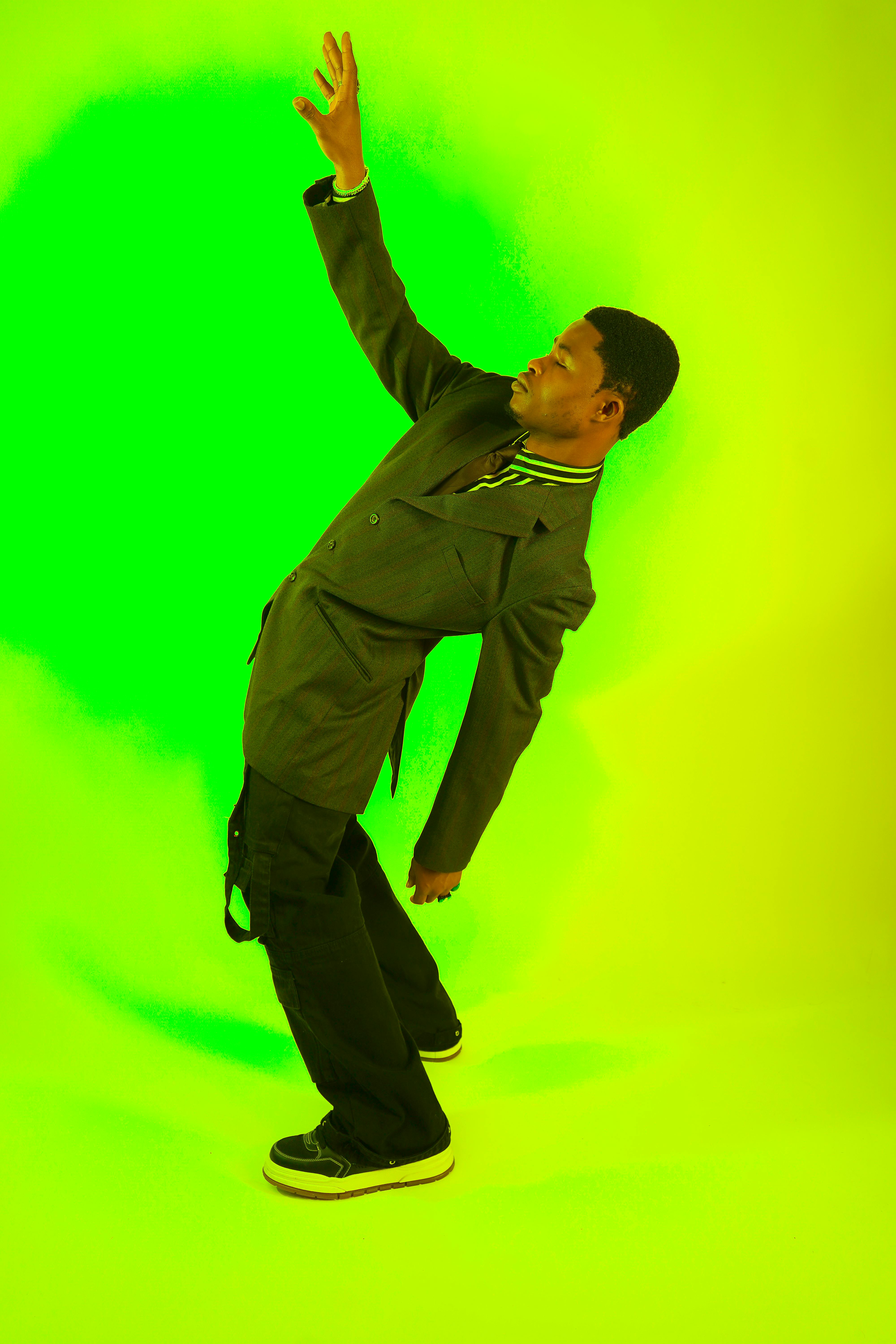 A stylish man poses with an arm raised in a vibrant green studio background.