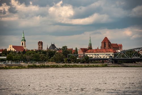Free A scenic view of a historic city with a river, featuring notable architecture and a bridge under cloudy skies. Stock Photo