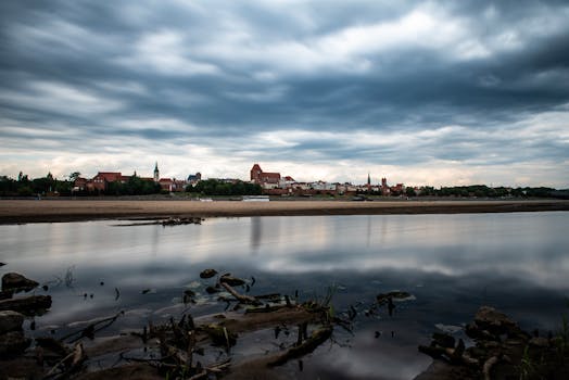 Gloomy, overcast sky reflecting over Toruń's historic skyline along the Vistula River.