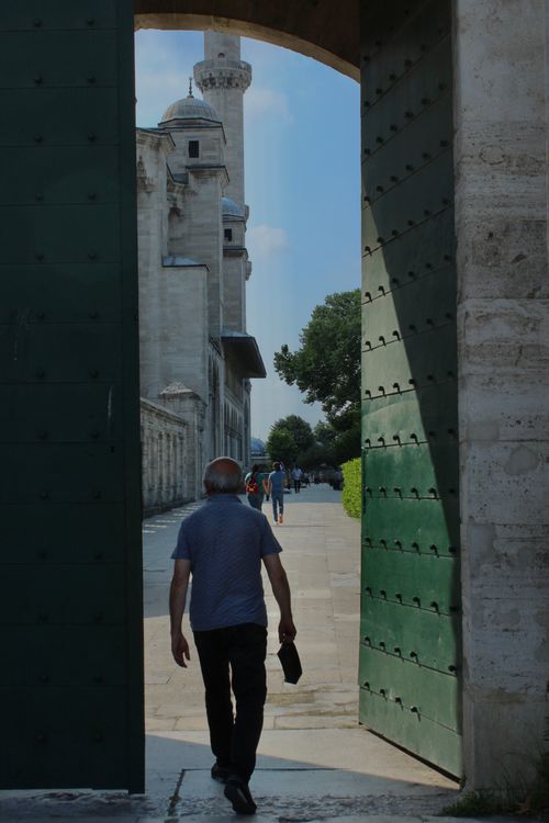 Free An elderly man walks through a large doorway towards a mosque, capturing urban life and architecture. Stock Photo