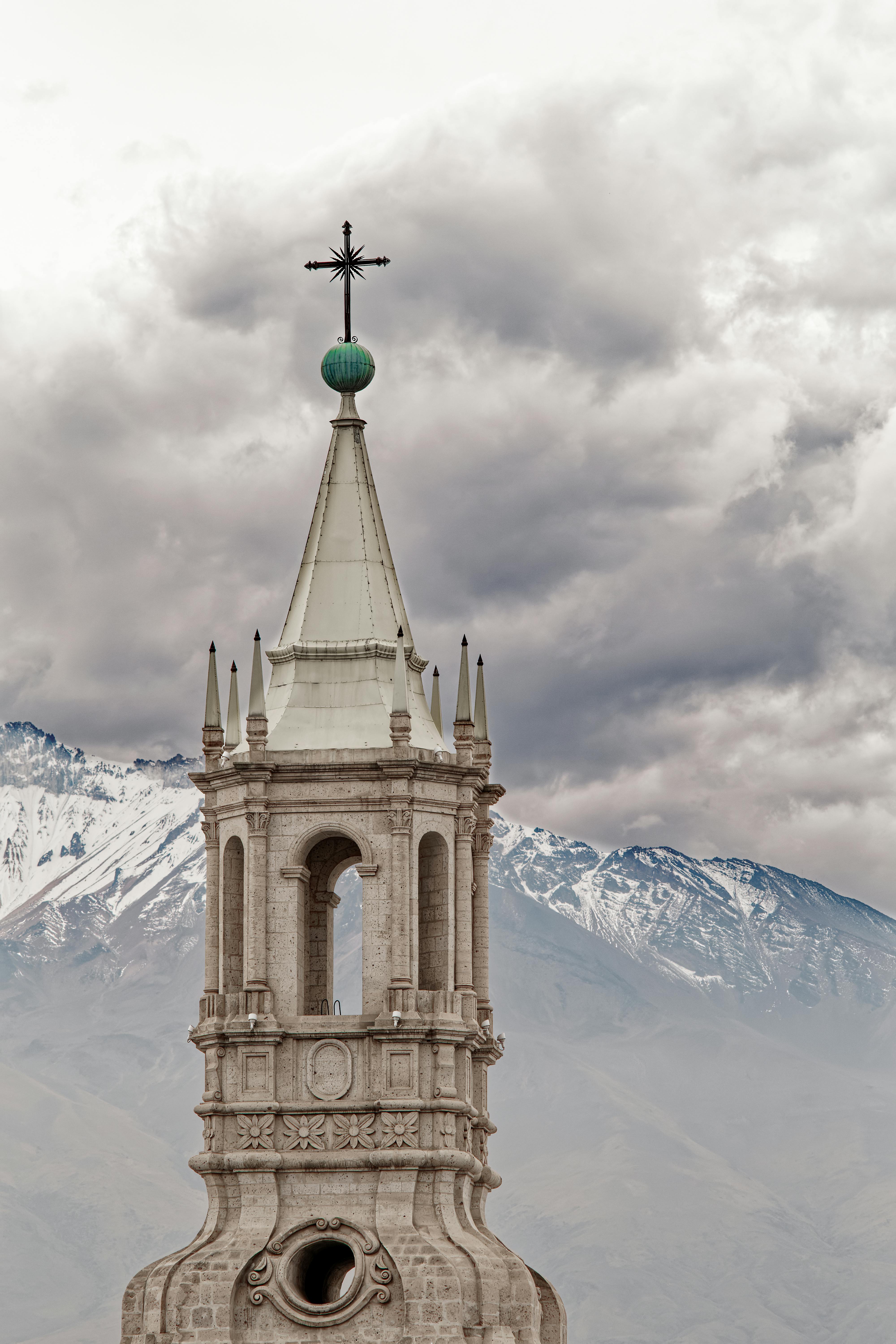 A stunning bell tower of a Gothic-style cathedral set against the Andes in Arequipa, Peru, under dramatic clouds.