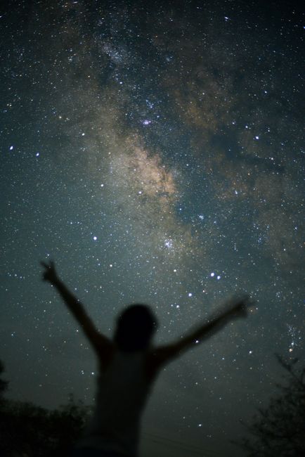 A person silhouette with arms raised against a clear starry night sky, showcasing the Milky Way.