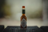 Close-up of a Tabasco sauce bottle on a wooden surface, emphasizing its spicy essence.