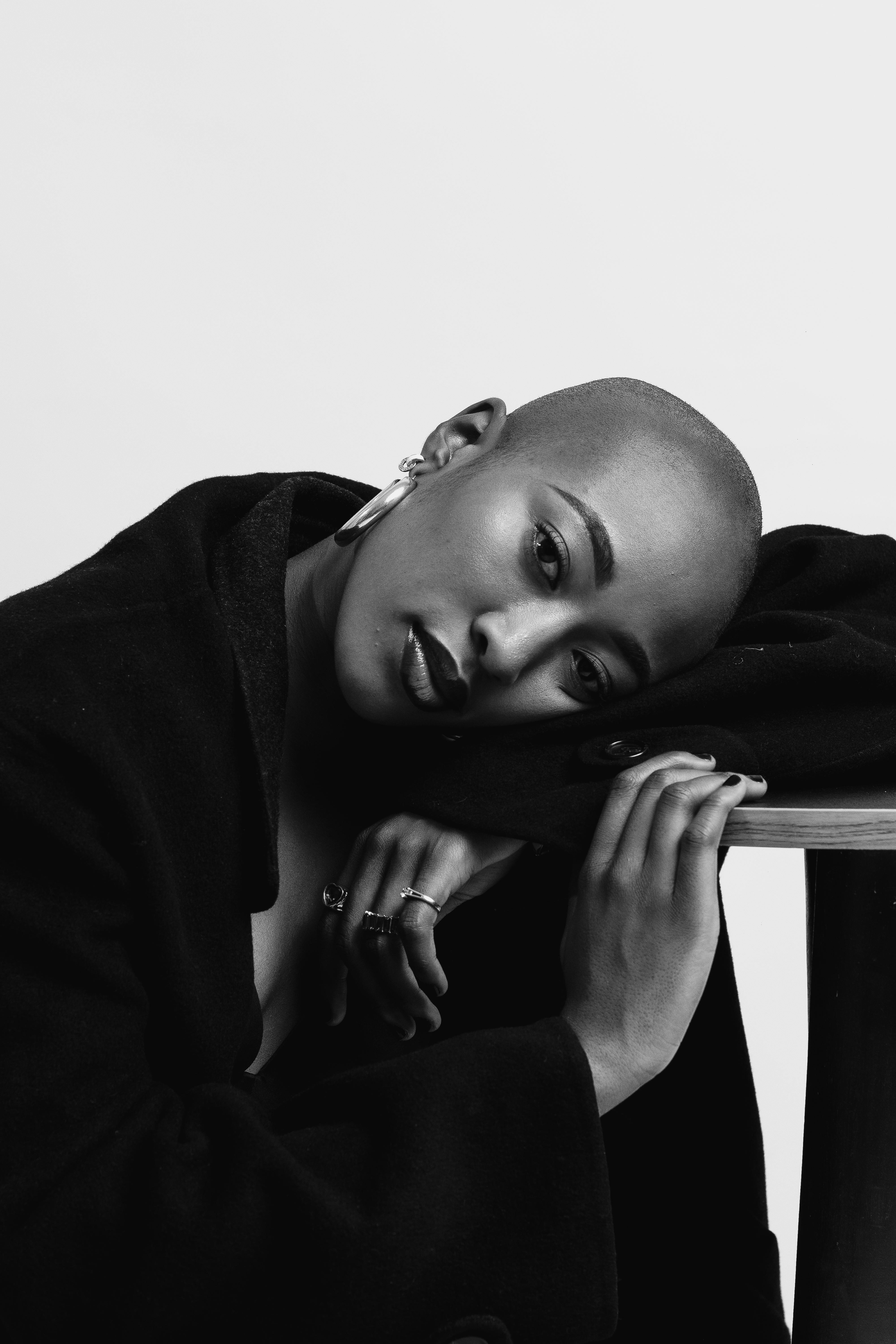 Minimalist black and white portrait of a bald woman with artistic pose and jewelry.