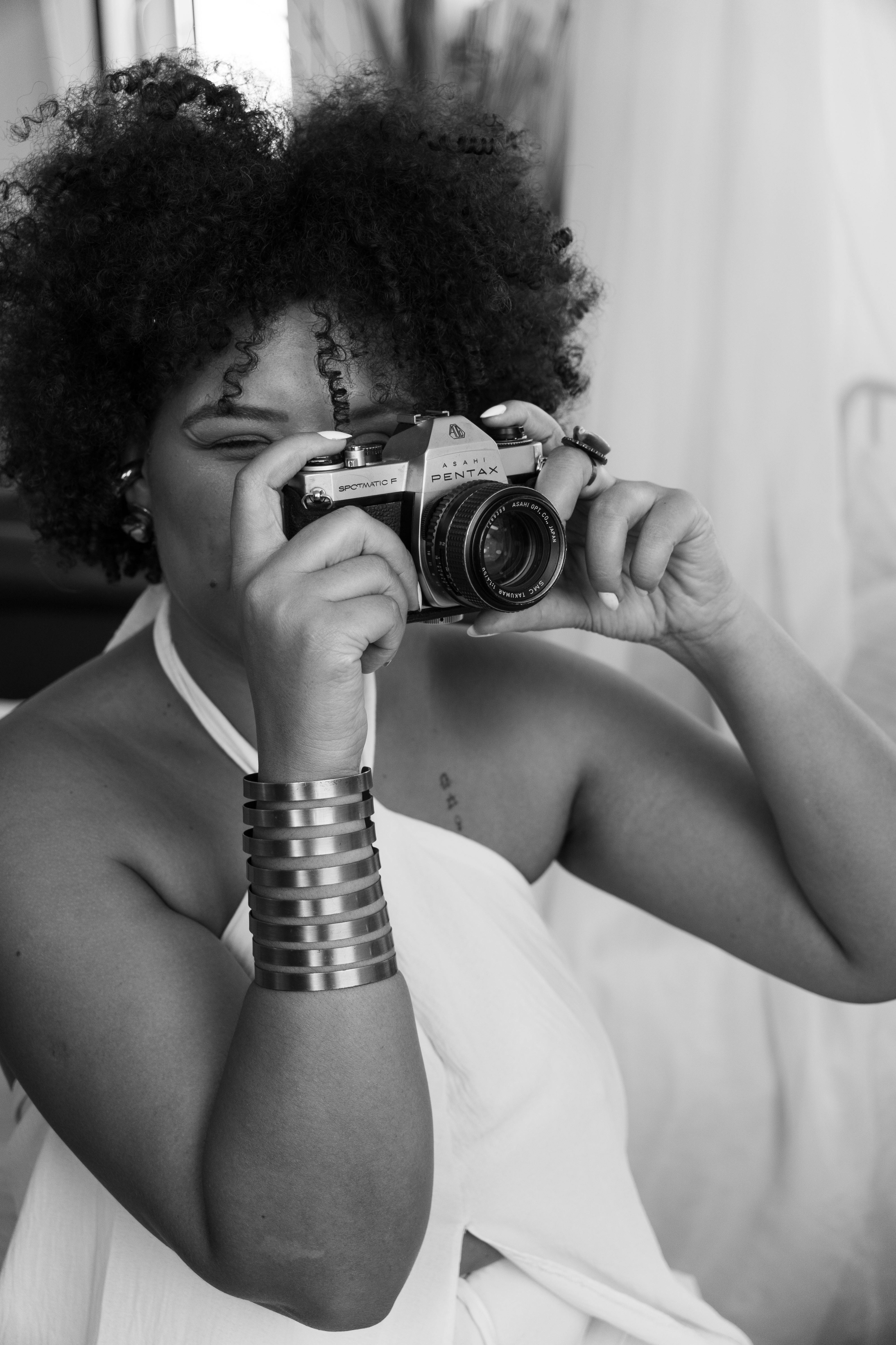 Black and white portrait of woman holding a vintage camera, showcasing elegant fashion and artistry.