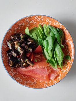 Top view of orange patterned bowl with salmon, eggplant, avocado, and spinach.
