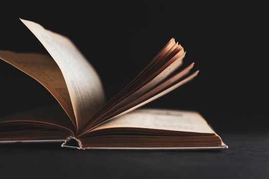 An artistic close-up of an open book with pages turning against a black background.