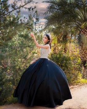 A woman in a stunning black dress stands elegantly in a lush forest setting.