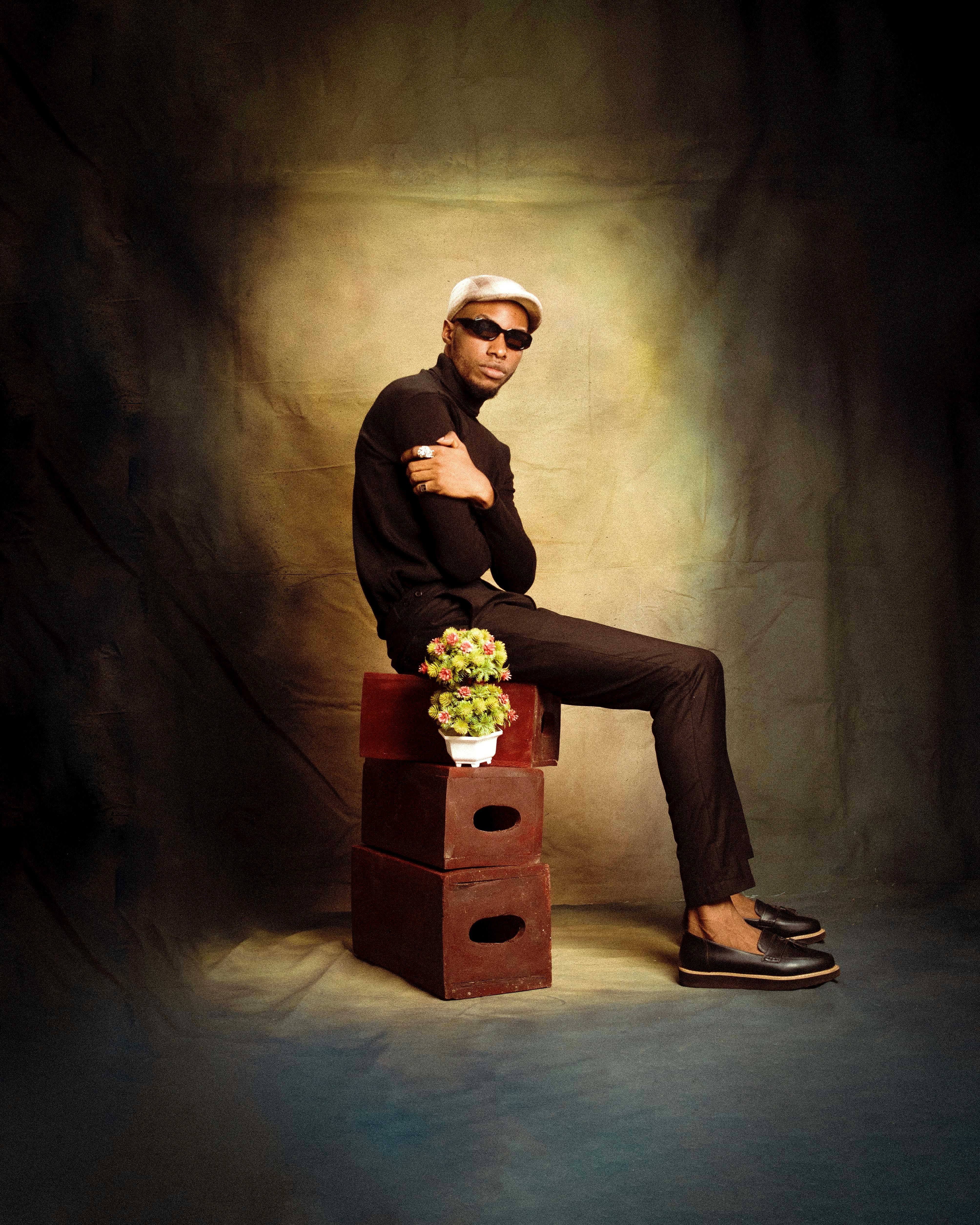 Fashionable man in black attire sitting on wooden boxes in studio setting.