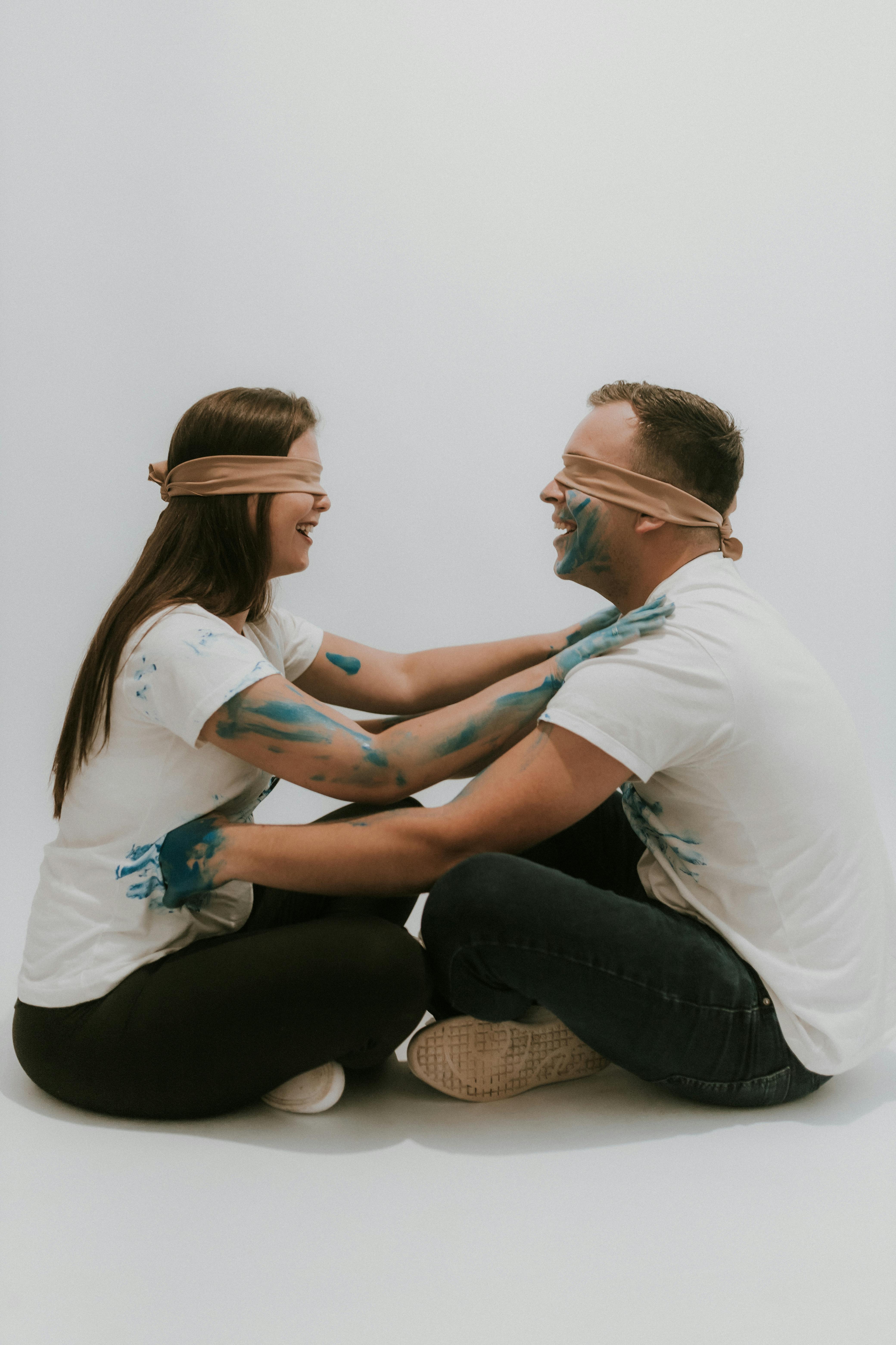 A fun and artistic studio portrait of a playful couple with paint and blindfolds, smiling and enjoying the moment.