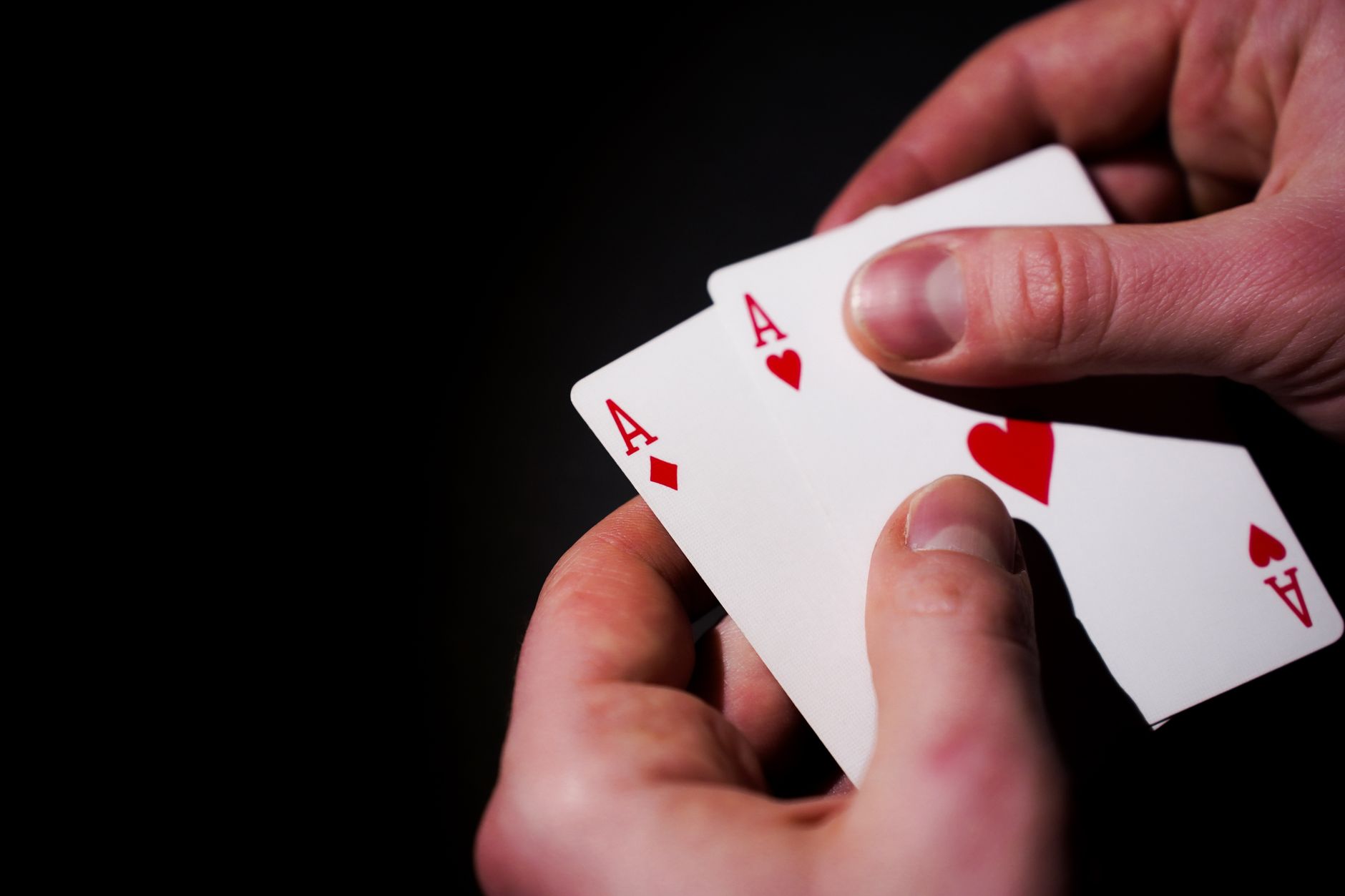 Hands holding three aces against a dark background, symbolizing luck and skill in card games.