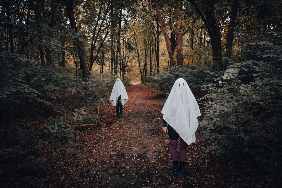 Two people dressed as ghosts in a forest during autumn, creating a haunting Halloween scene.