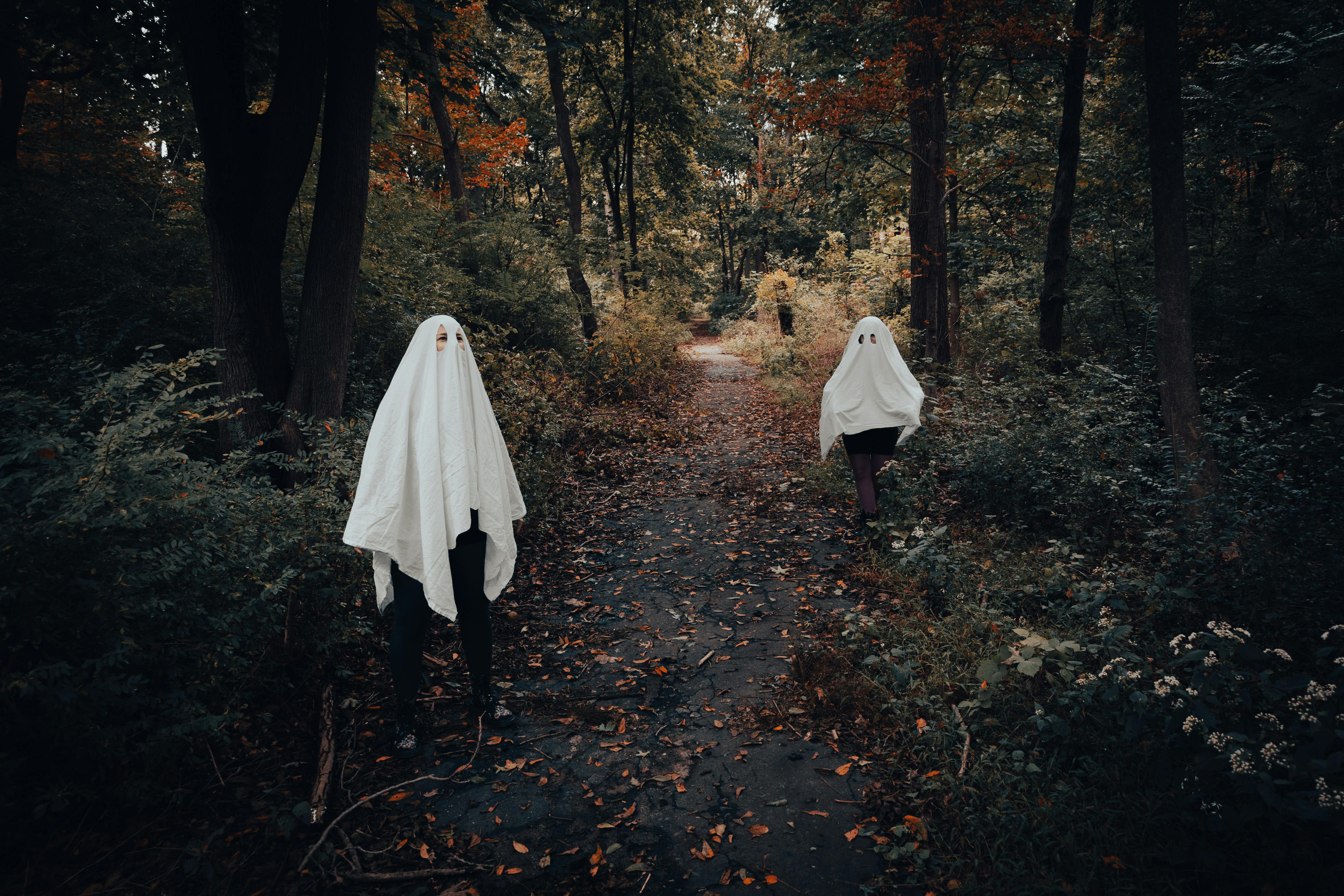 Two people dressed as ghosts wandering a forest path during fall.