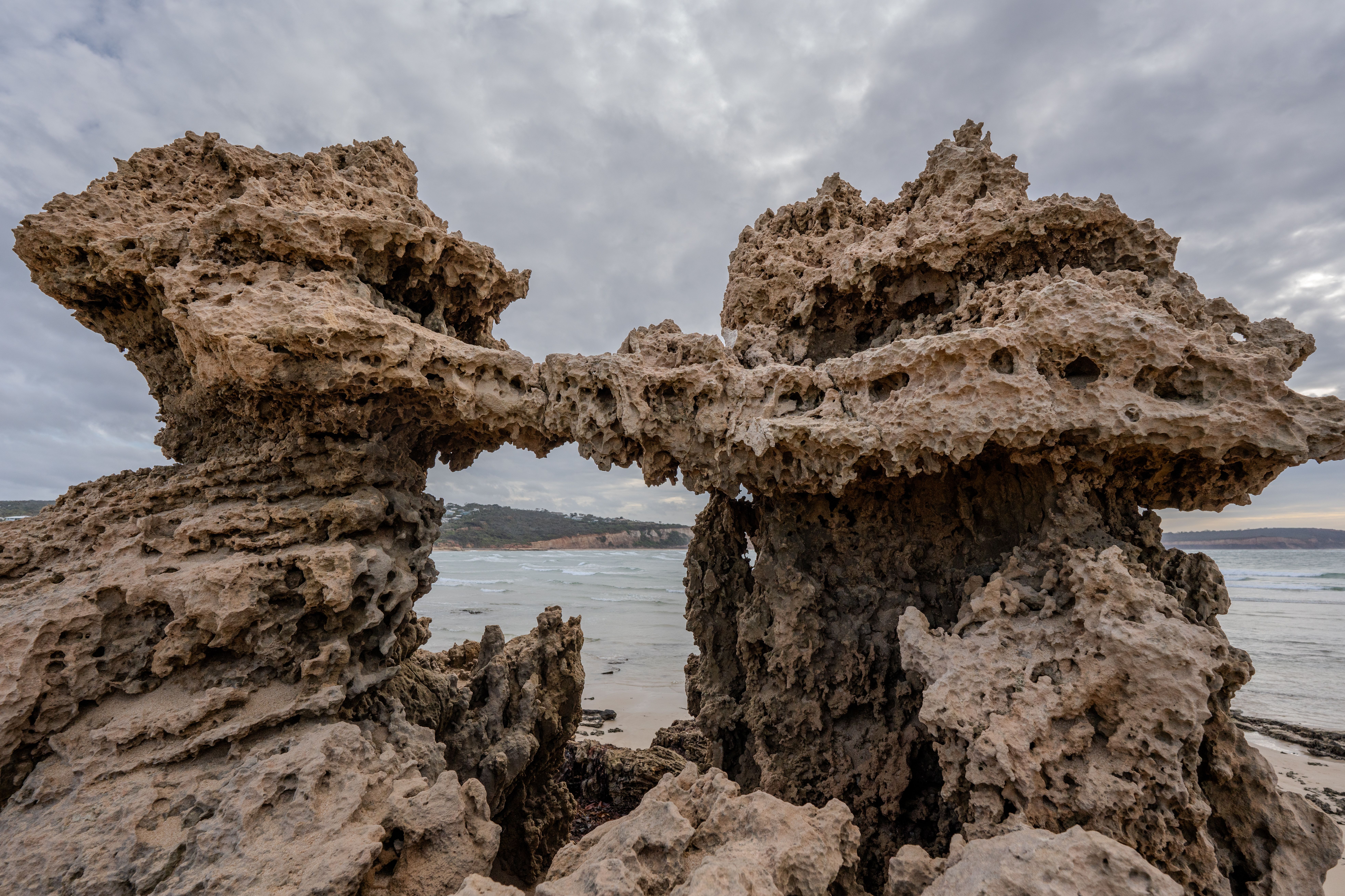 A striking coastal rock formation displaying natural erosion against a cloudy backdrop by the sea.