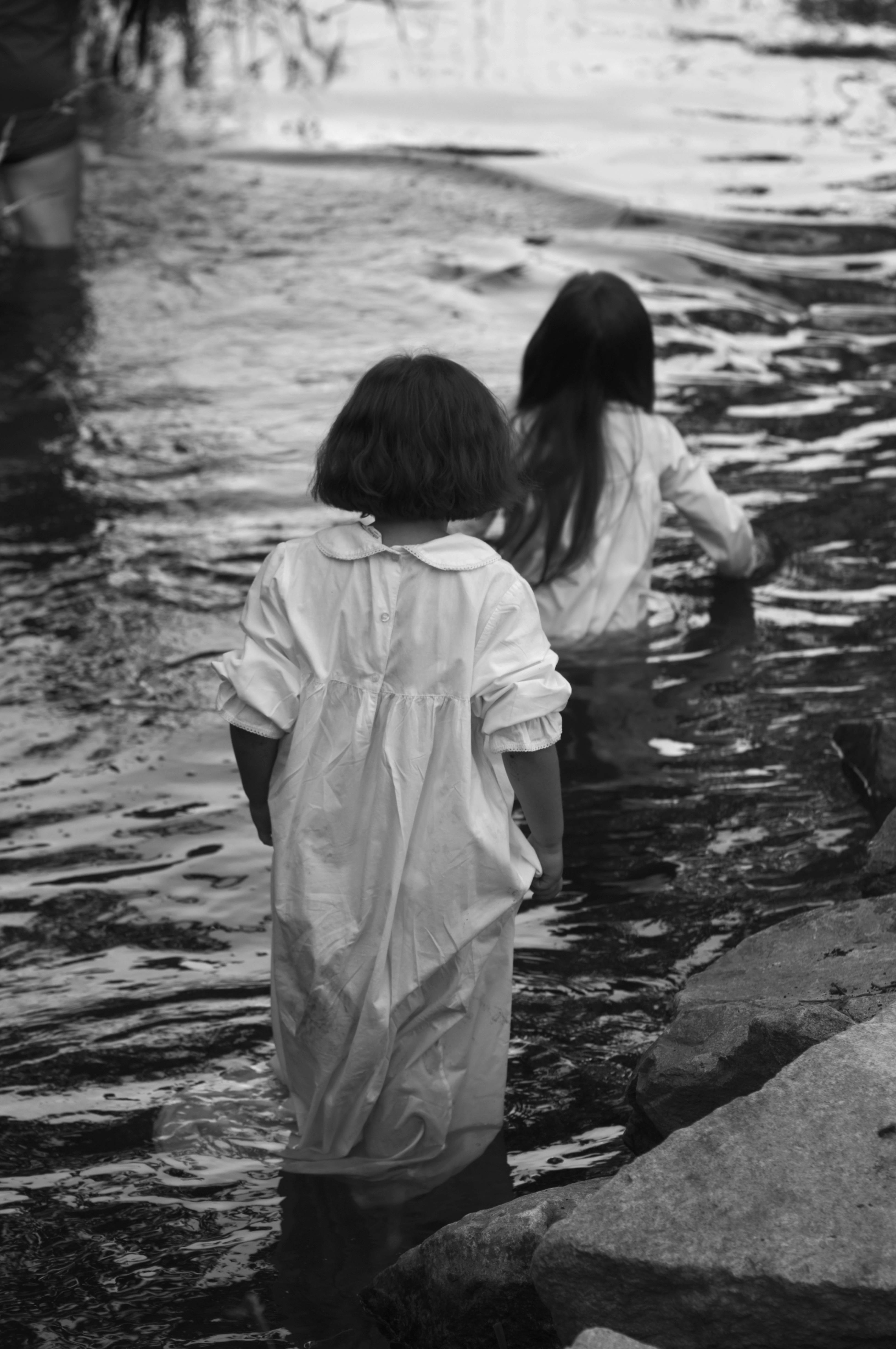 Two children wade through a peaceful stream, captured in a timeless black and white photo.