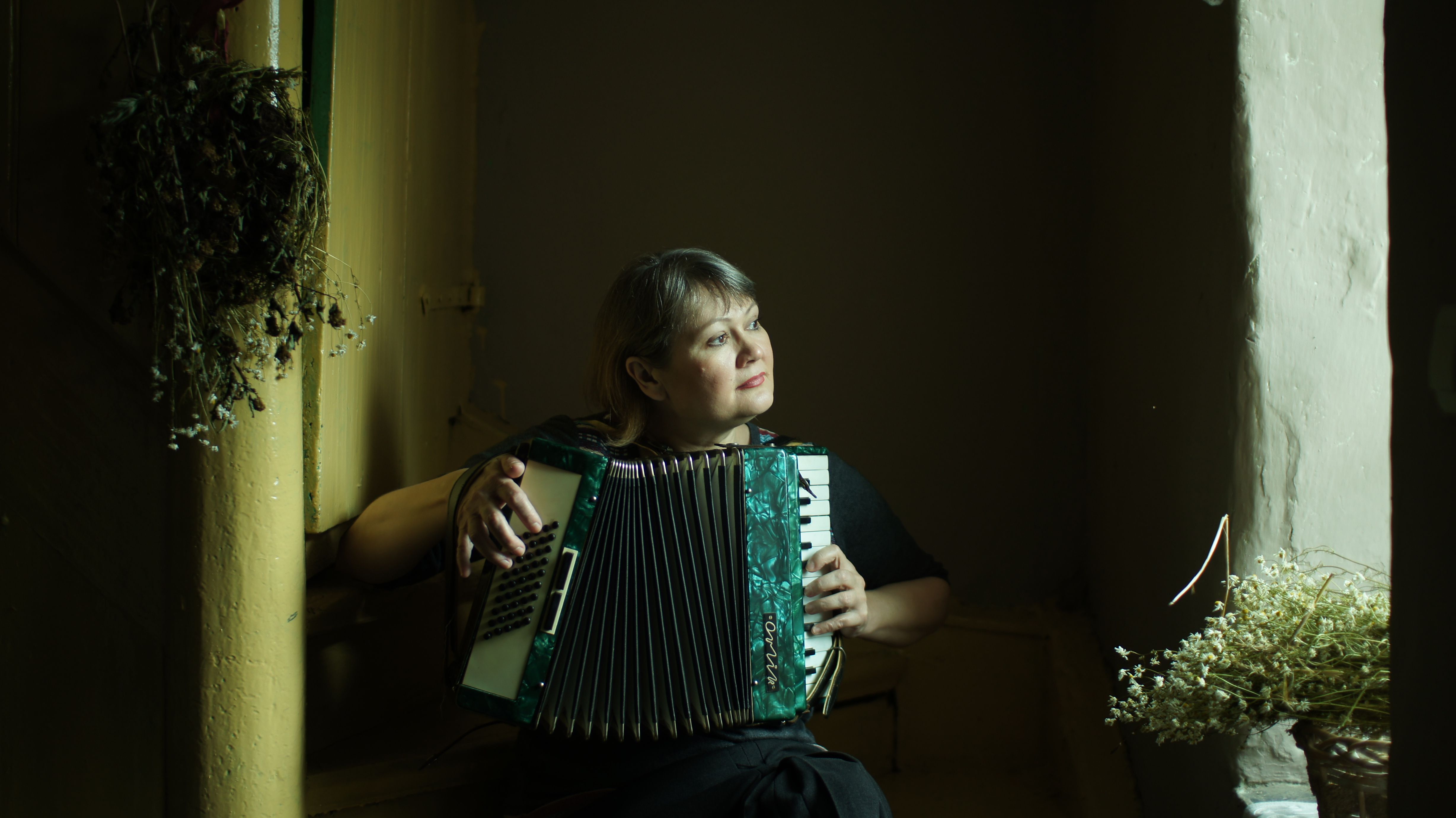 A woman playing an accordion in a dimly lit room, creating a serene and introspective mood.