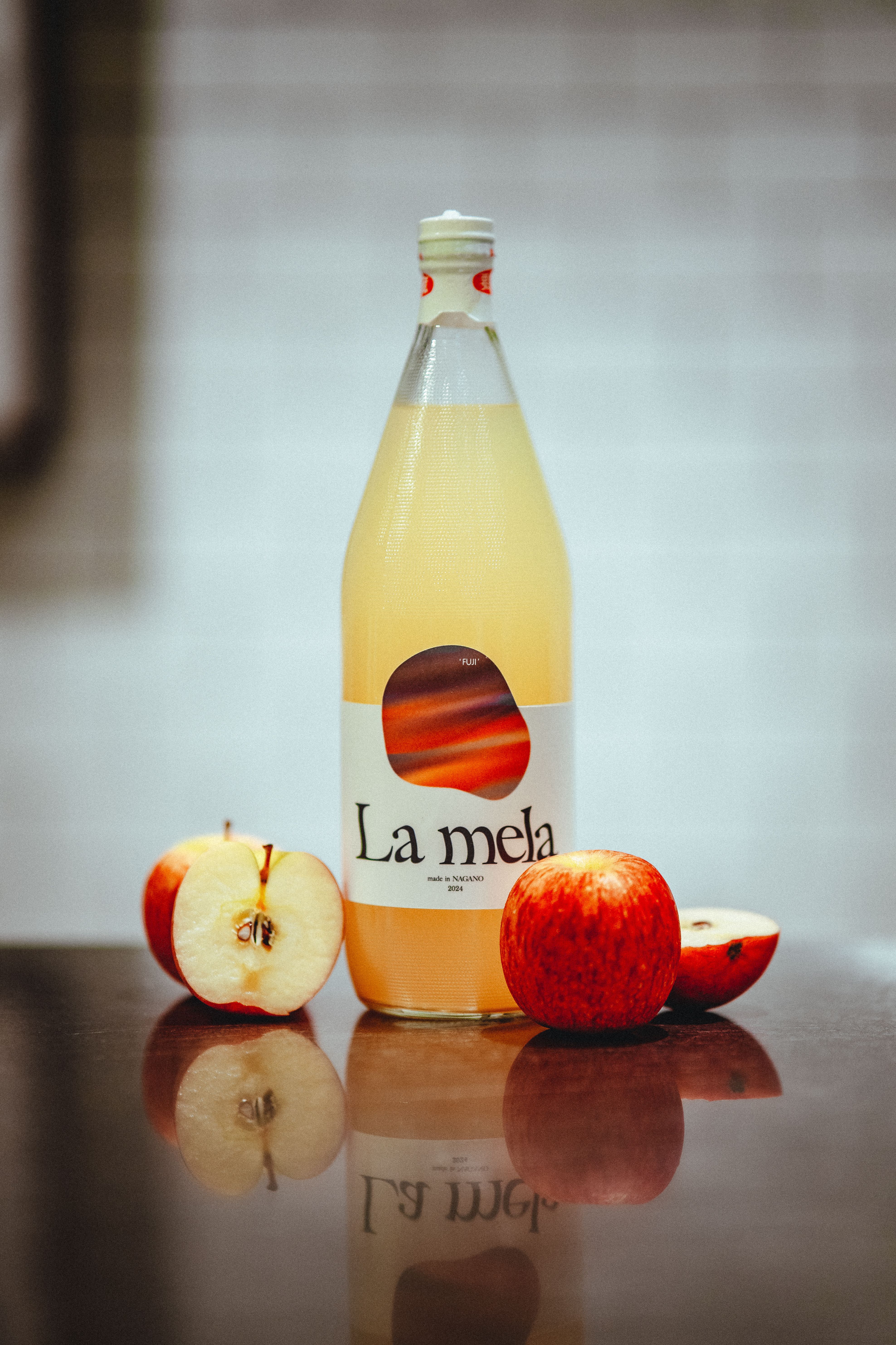Refreshing apple juice in a glass bottle surrounded by whole and sliced apples on a reflective surface.