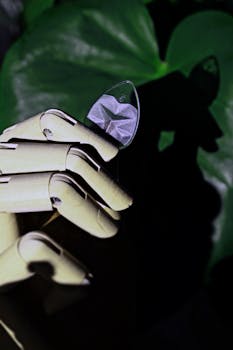 Close-up of a wooden robotic hand holding a guitar pick against a green background.