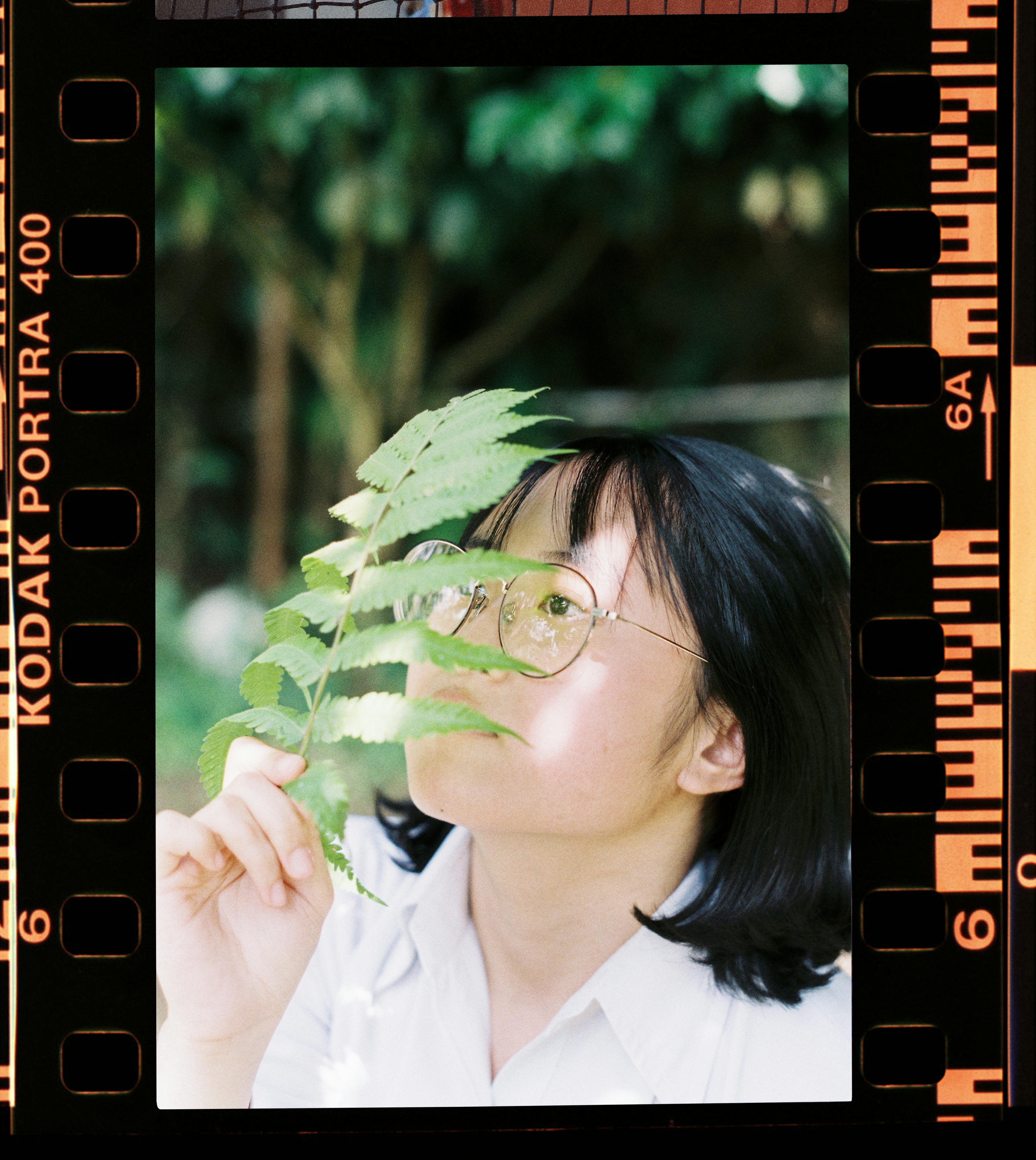 Portrait of a young woman with glasses holding a fern outdoors.