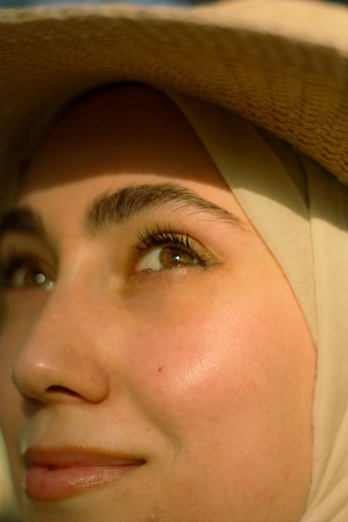 Free A close-up portrait of a woman in a hat and headscarf, smiling in sunlight. Stock Photo
