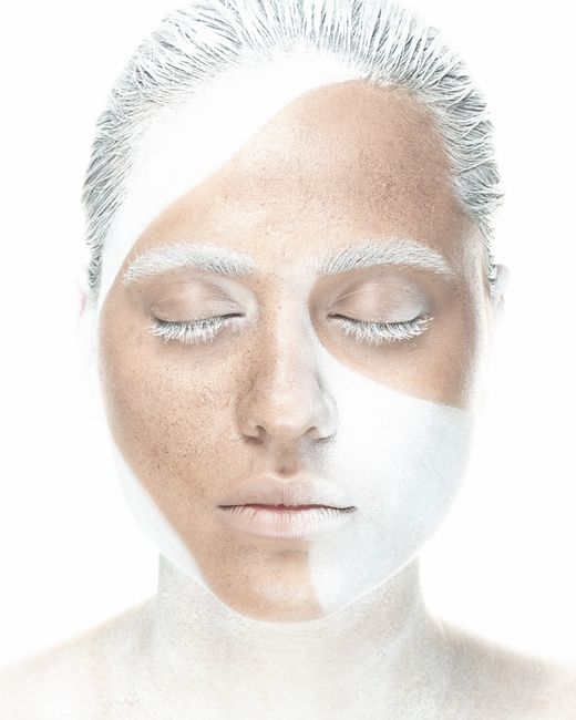 Artistic high key portrait of a woman with white makeup and serene expression, highlighting purity and beauty.