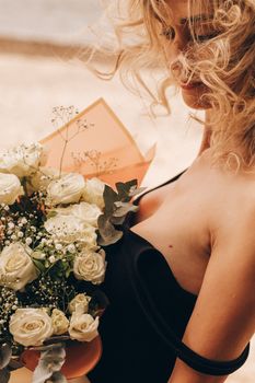 A woman in black dress holding a bouquet of white roses by the beach