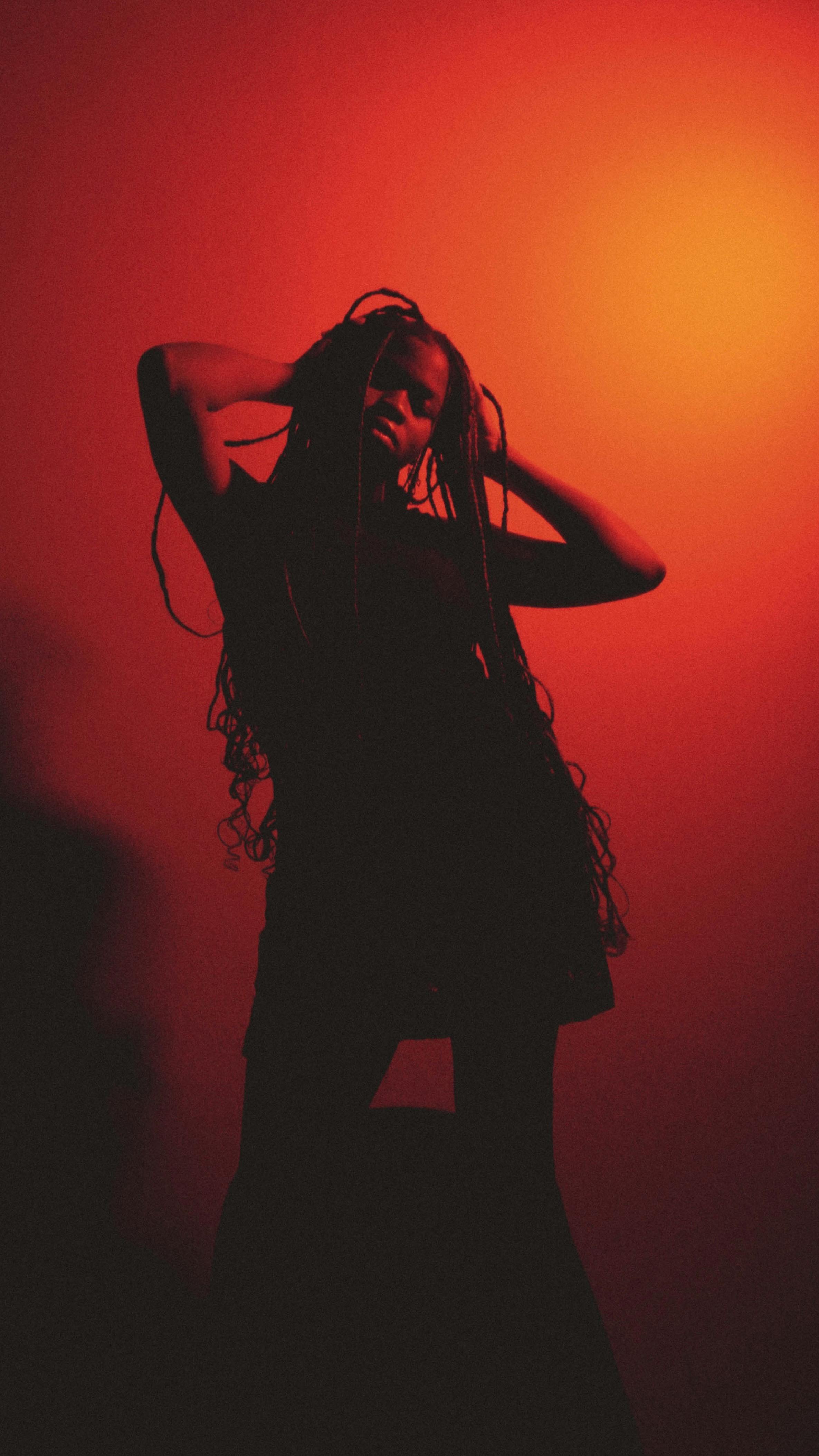 A fashionable portrait of a woman striking a pose against a vivid red background in a studio setting.